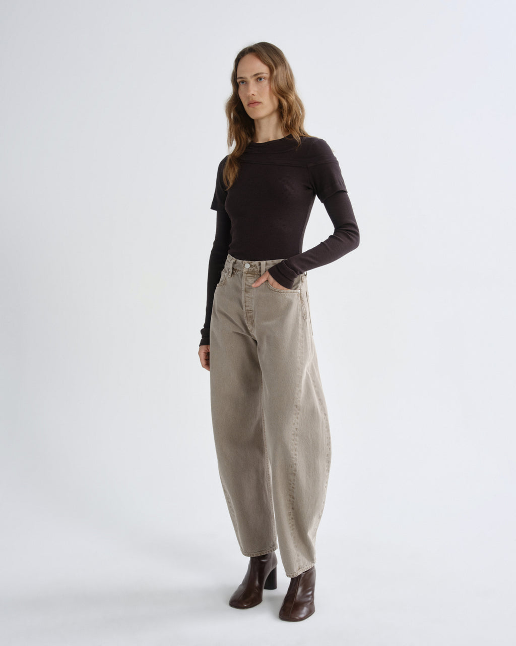 Person wearing brown layered t-shirt with khaki pants and brown boots on a grey background