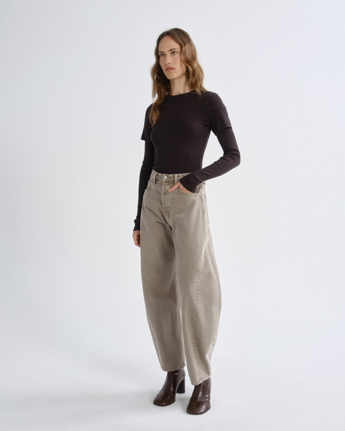 Person wearing brown layered t-shirt with khaki pants and brown boots on a grey background