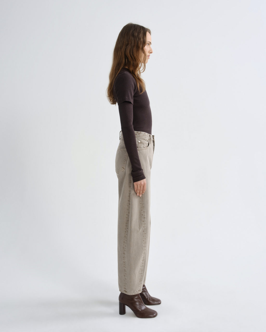 Person wearing brown layered t-shirt with khaki pants and brown boots on a grey background