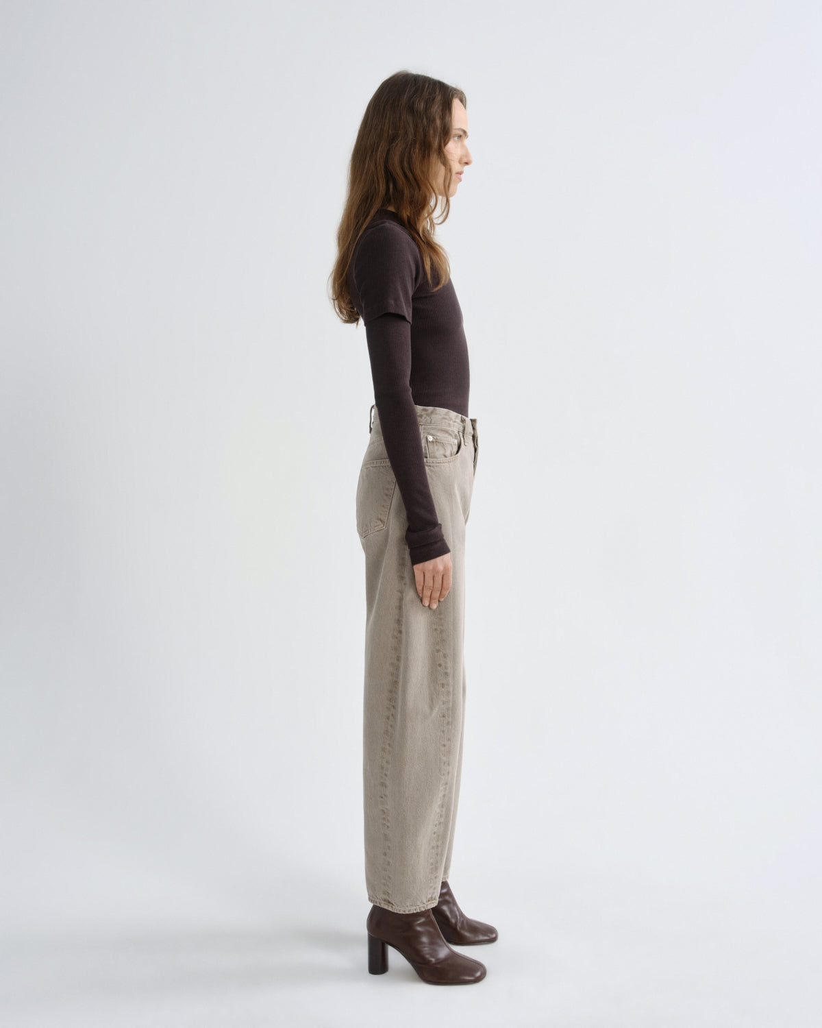 Person wearing brown layered t-shirt with khaki pants and brown boots on a grey background