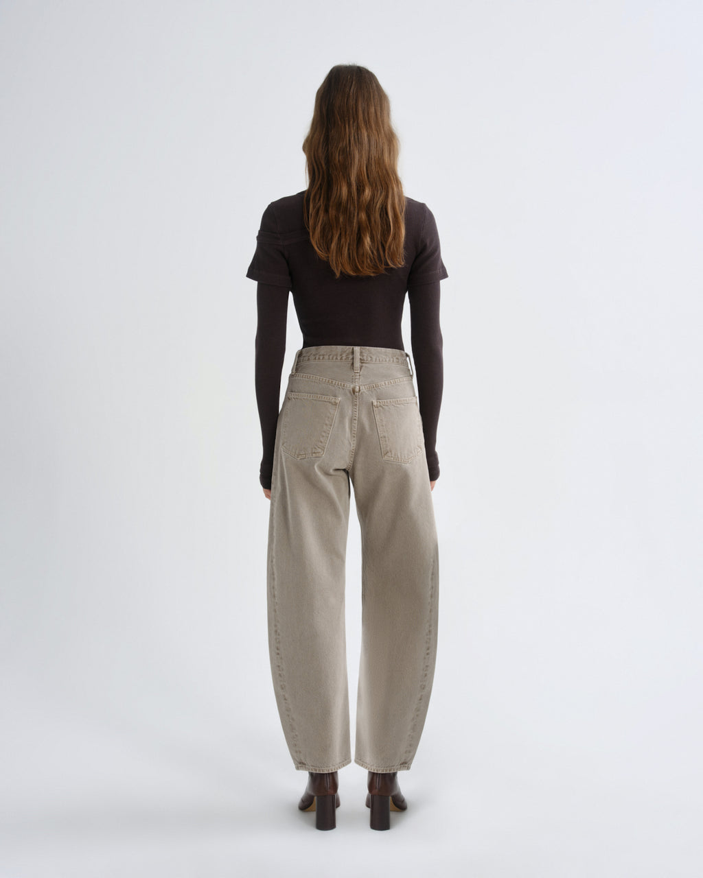 Person wearing brown layered t-shirt with khaki pants and brown boots on a grey background