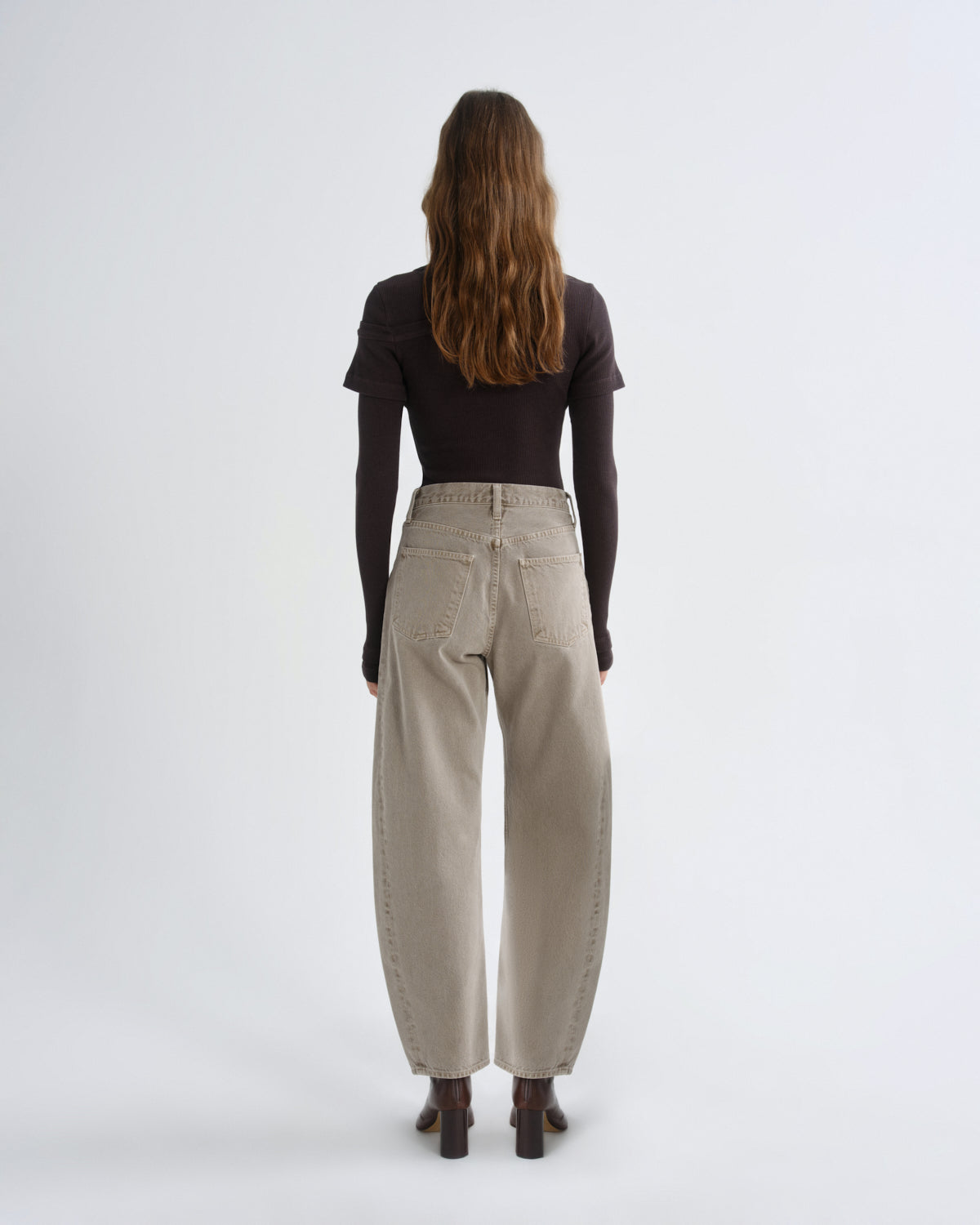 Person wearing brown layered t-shirt with khaki pants and brown boots on a grey background
