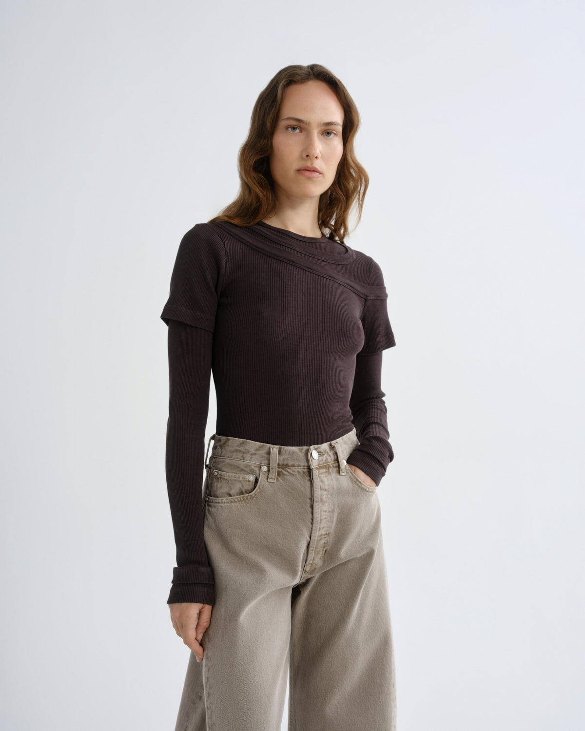 Close up of person wearing brown layered t-shirt with khaki pants on a grey background
