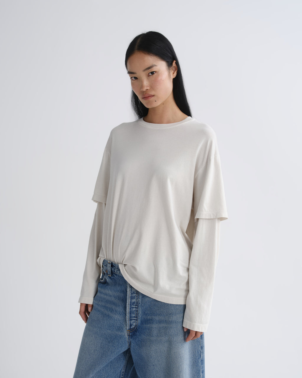 Woman wearing a white sweater and blue jeans on a plain background