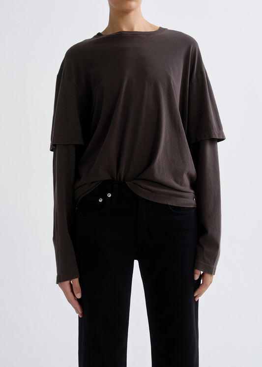 Person wearing a dark brown layered long sleeve top on a grey background.