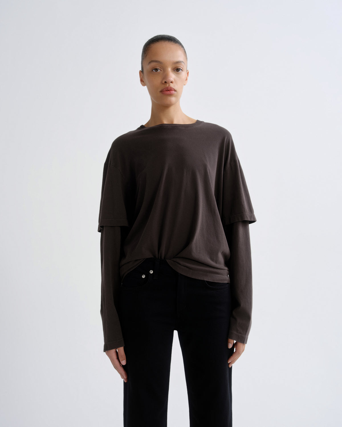 Person wearing a brown long-sleeve top and black pants on a white background