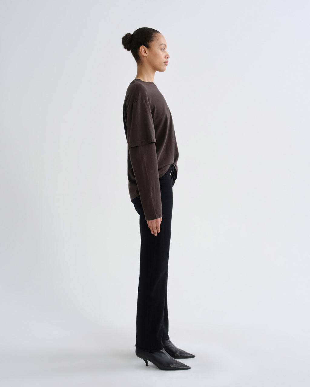 Person wearing a brown sweater and black pants on a white background