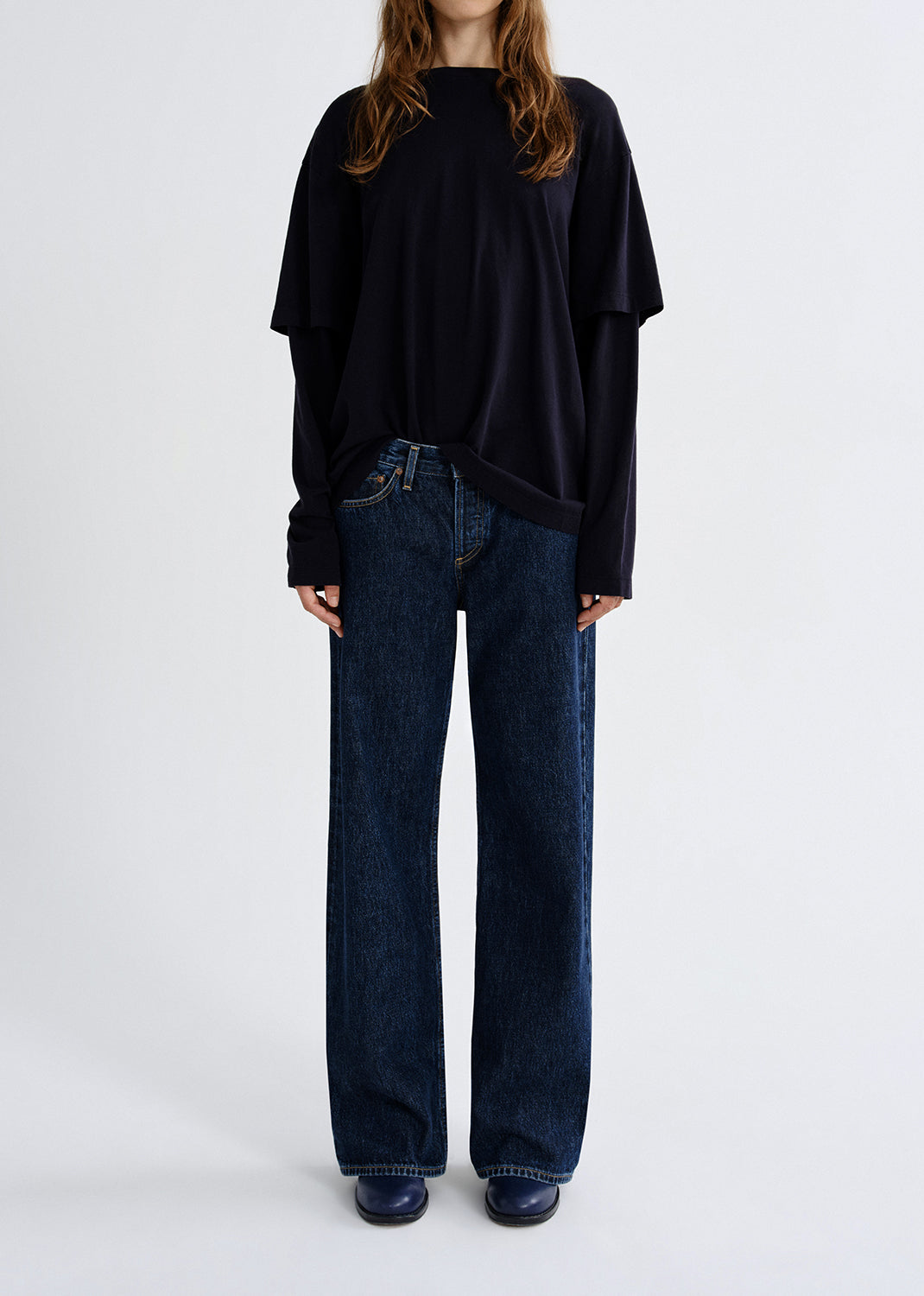 Person wearing a navy layered long sleeve top with dark wash wide leg jeans on a grey background.