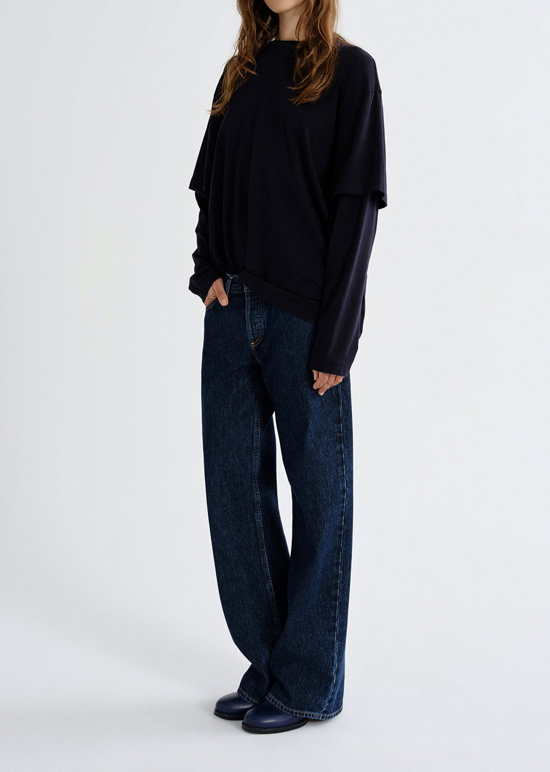 Person wearing a navy layered long sleeve top with dark wash wide leg jeans on a grey background.