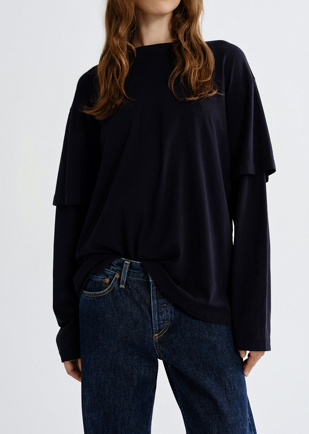Person wearing a navy layered long sleeve top on a grey background.