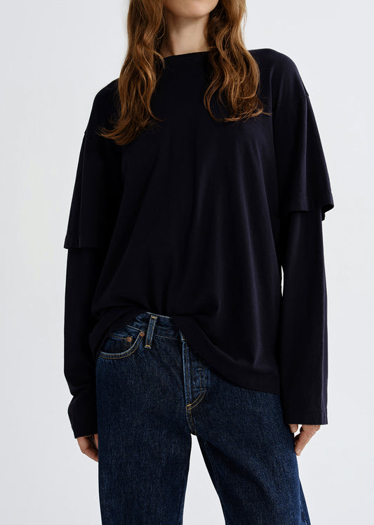 Person wearing a navy layered long sleeve top on a grey background.