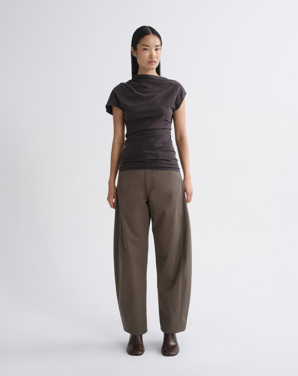 Person wearing a dark brown draped cap sleeve top with olive wide leg pants on a grey background