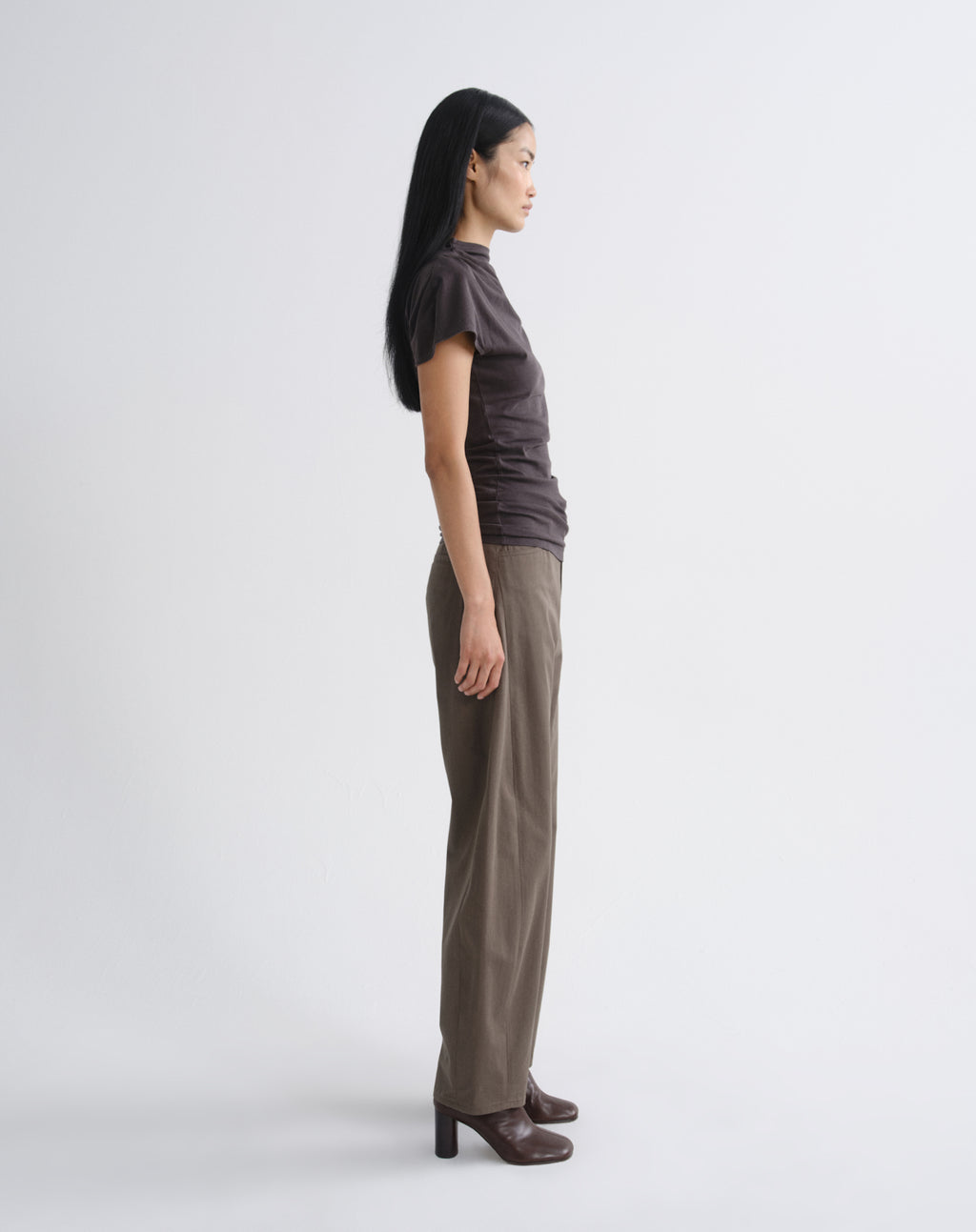 Person wearing a dark brown draped cap sleeve top with olive wide leg pants viewed from the side on a grey background