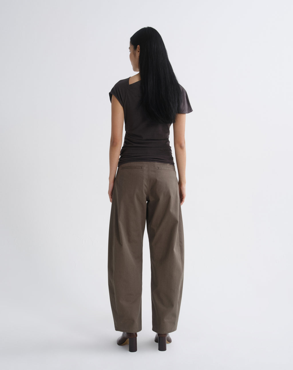 Person wearing a dark brown draped cap sleeve top with olive wide leg pants viewed from the back on a grey background