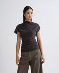 Person wearing a dark brown draped cap sleeve top with olive wide leg pants on a grey background