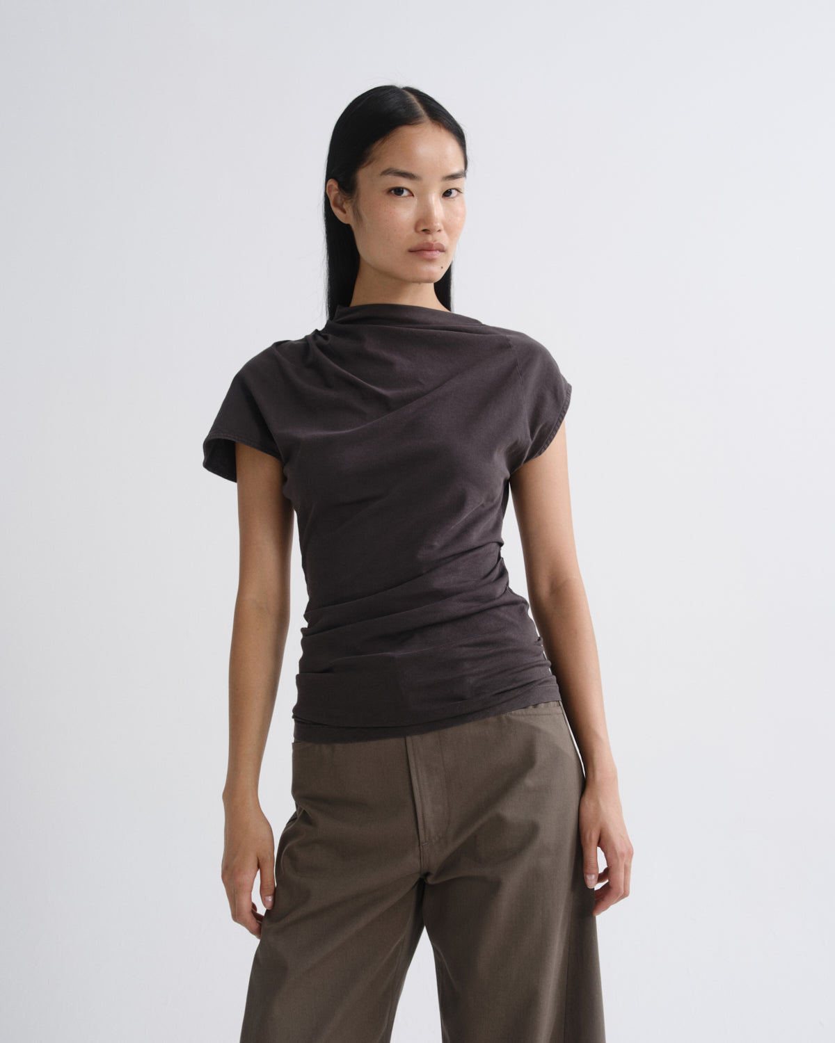 Person wearing a dark brown draped cap sleeve top with olive wide leg pants on a grey background