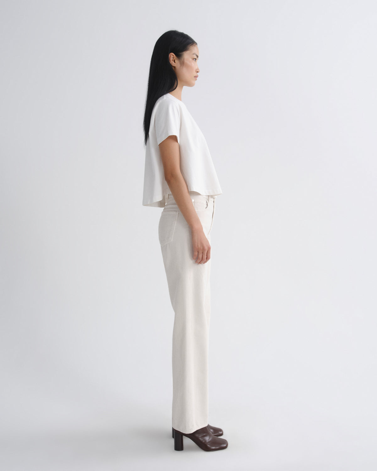Woman wearing a white top and beige pants on a plain background