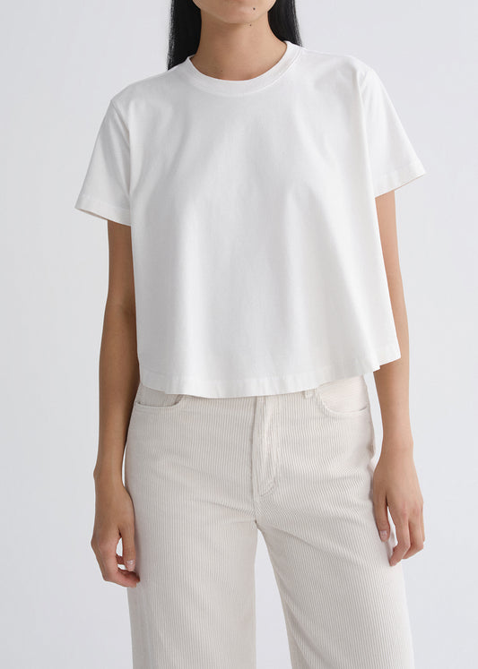 A model wearing a white short-sleeve cropped t-shirt and off-white corduroy trousers, shown from the neck down against a grey background.