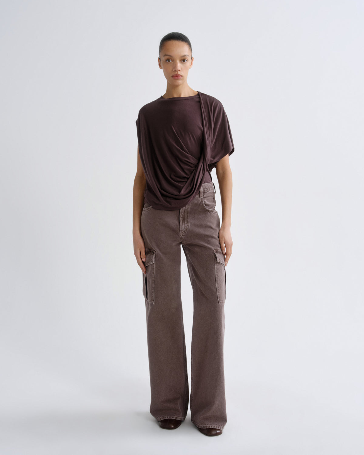 Person wearing a dark purple top and pants on a grey background