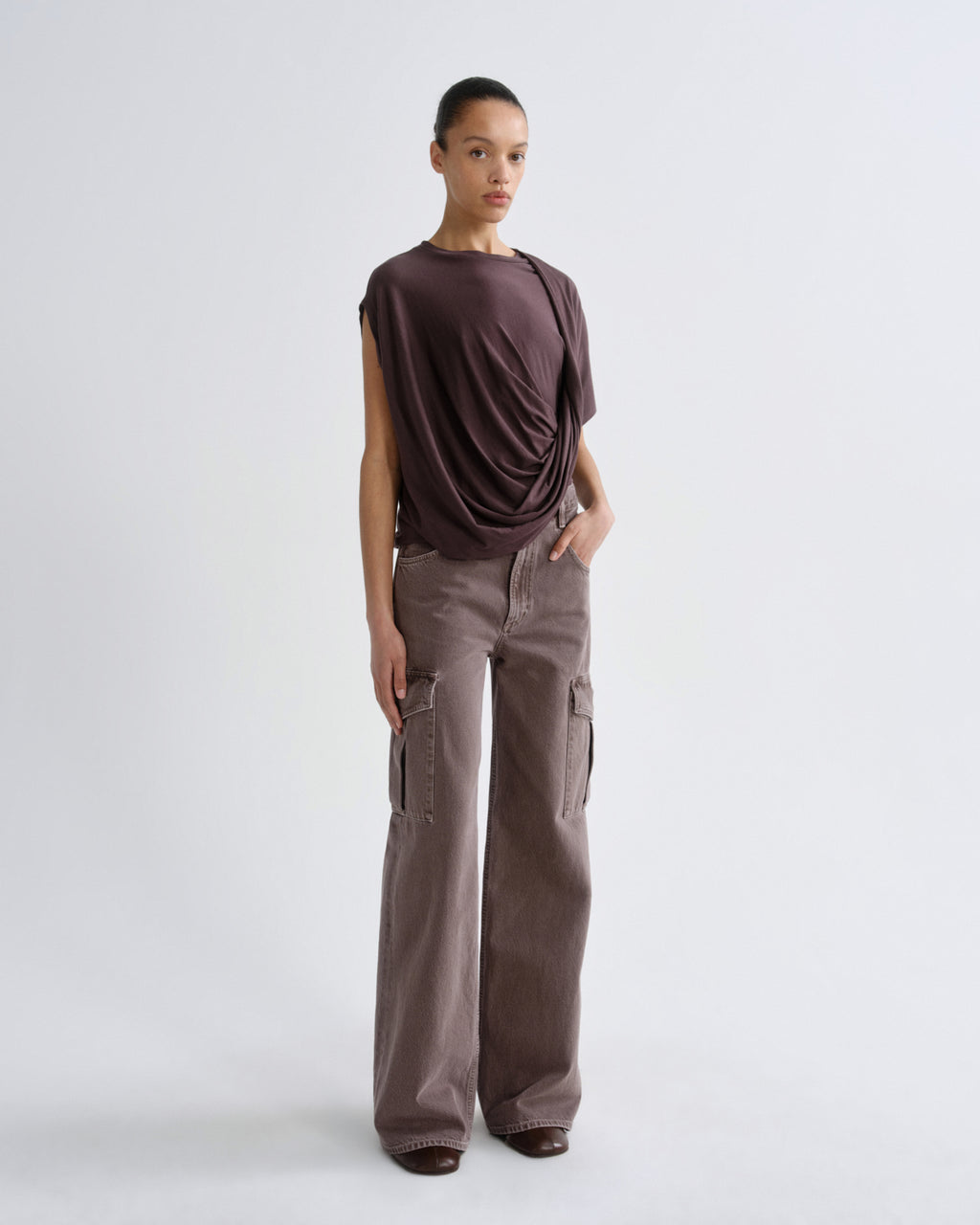 Woman wearing a dark purple top and cargo pants on a grey background