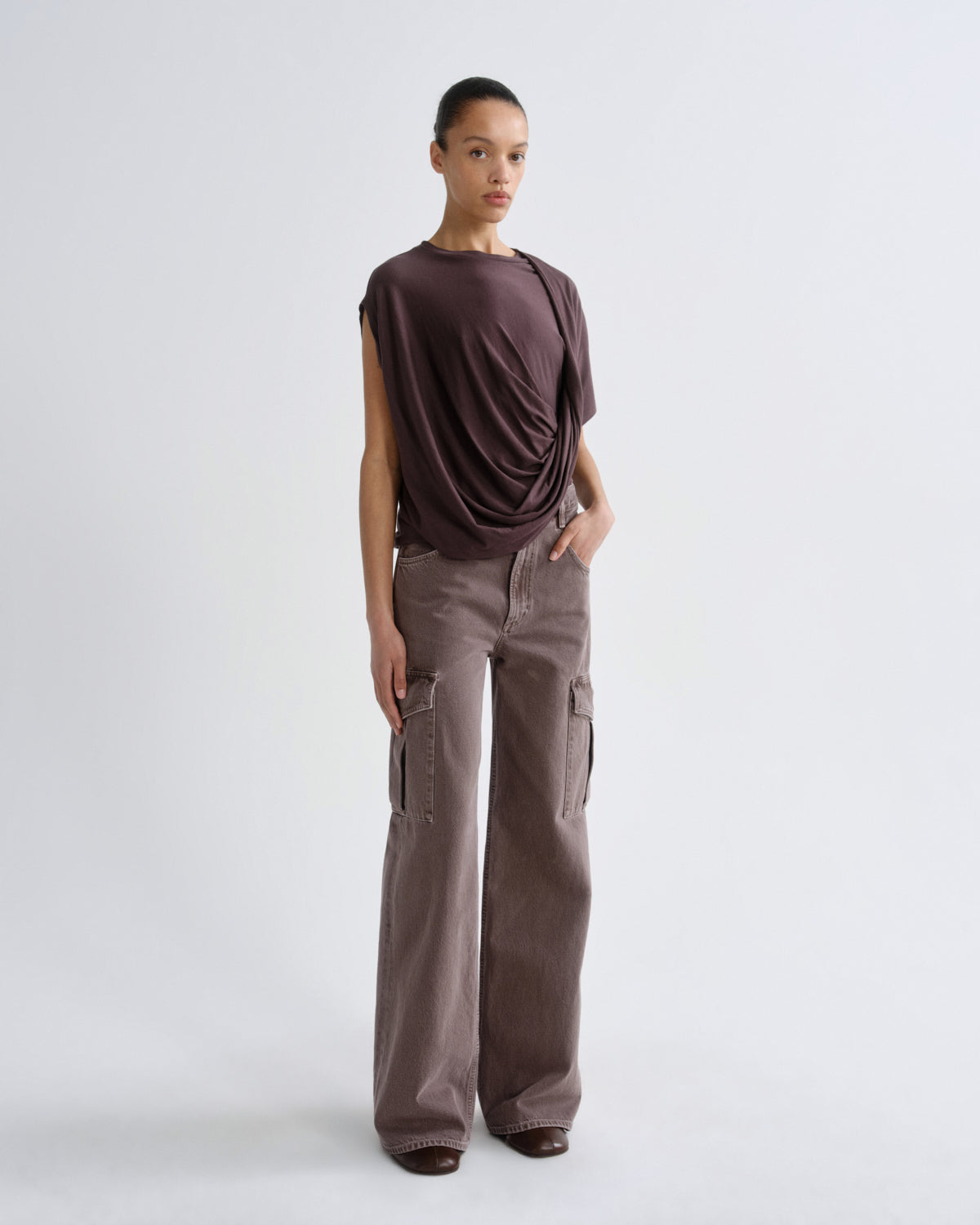 Woman wearing a dark purple top and cargo pants on a grey background