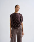 Person wearing a dark purple draped top and cargo pants on a grey background