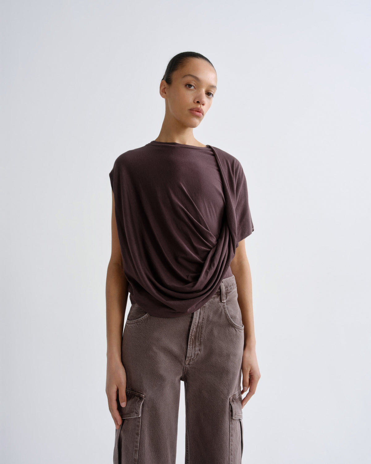 Person wearing a dark purple draped top and cargo pants on a grey background