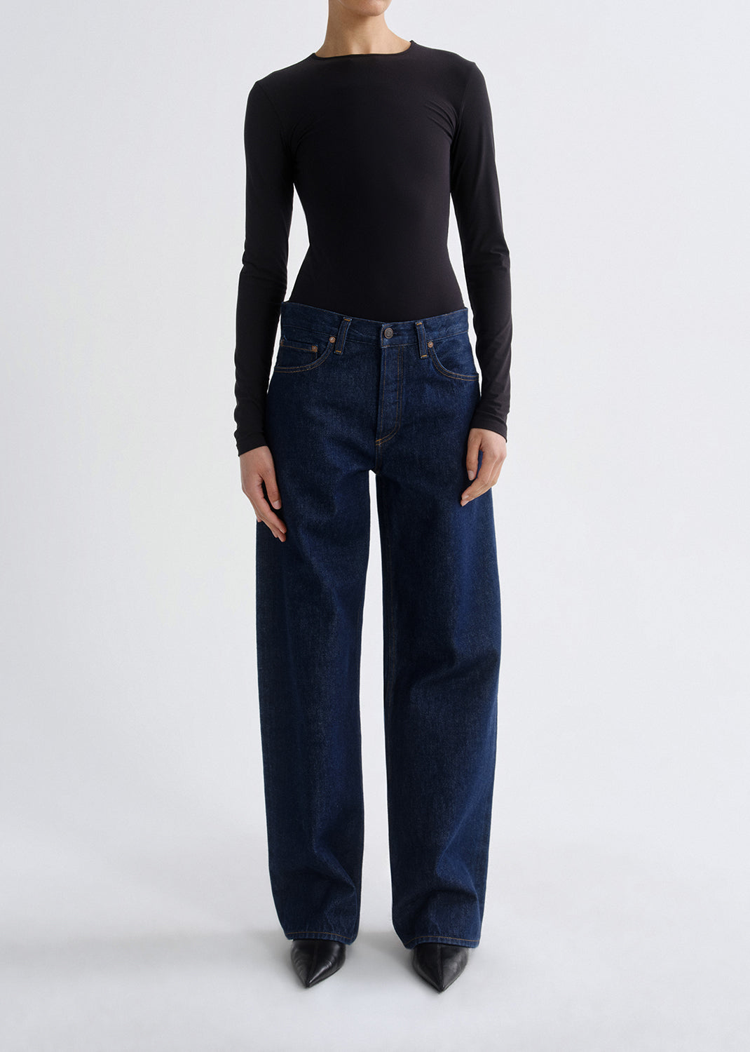 A model wearing a black long-sleeve top and dark blue wide-leg jeans, standing against a grey background.
