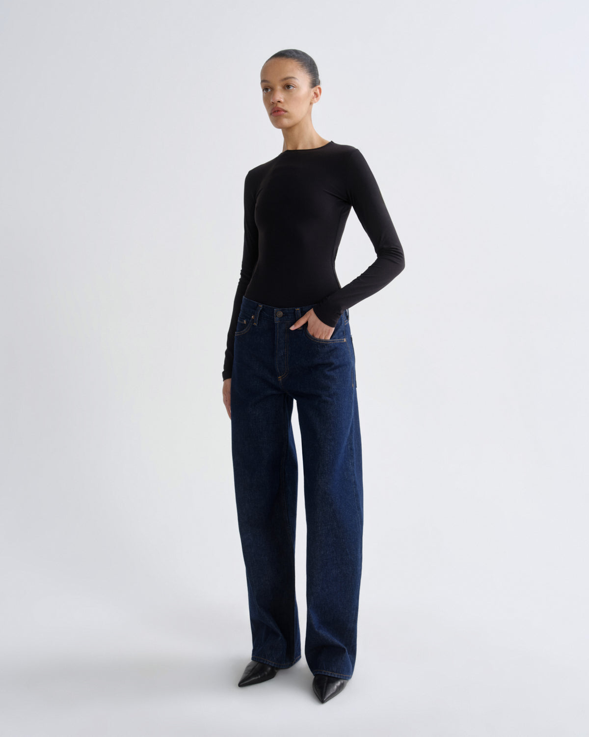 Person wearing a black long-sleeve top and dark blue jeans on a white background