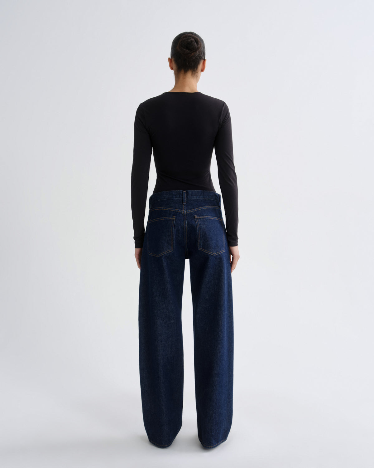 Person wearing dark blue jeans and a black long-sleeve top on a white background