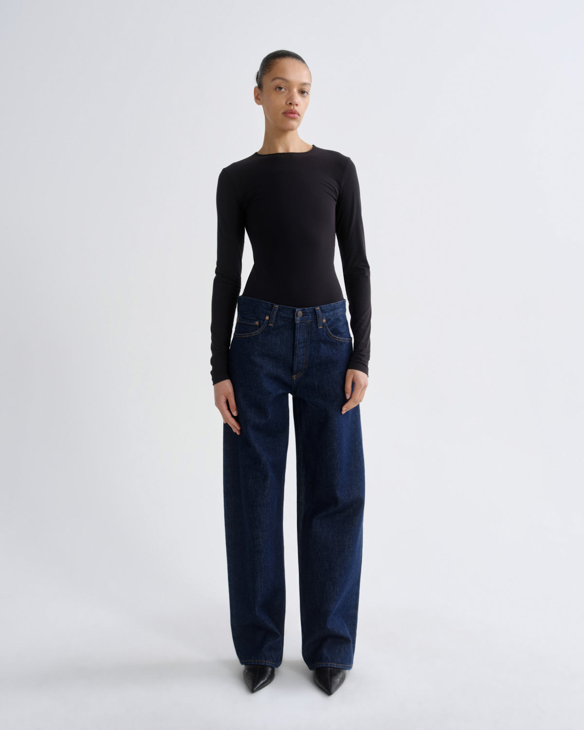 Person wearing a black long-sleeve top and dark blue jeans on a white background