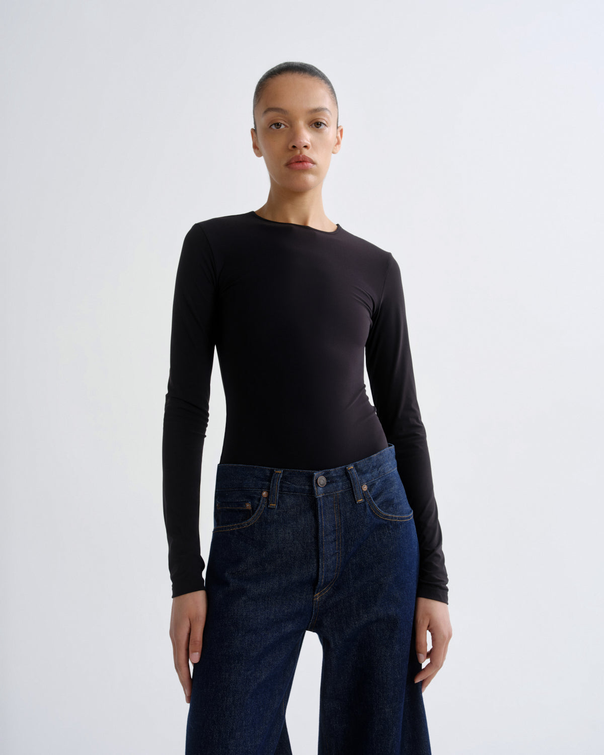 Person wearing a black long-sleeve top and blue jeans on a white background