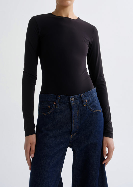A model wearing a black long-sleeve crewneck top and dark blue jeans, cropped from the neck down against a grey background.