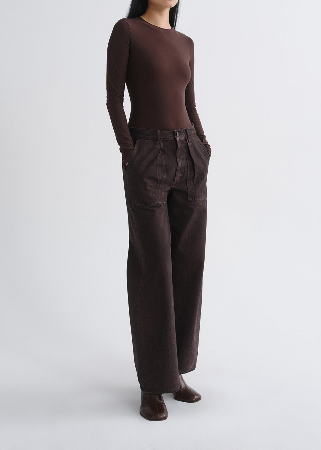 A model wearing a dark brown long-sleeve crewneck top and matching dark brown wide-leg trousers, standing against a grey background.