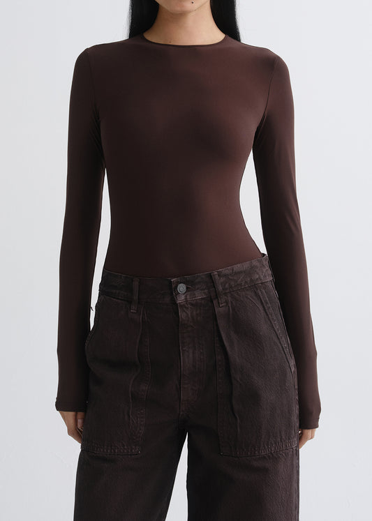 A model wearing a dark brown long-sleeve crewneck top and dark brown high-waisted pants, shown from the neck down against a grey background.