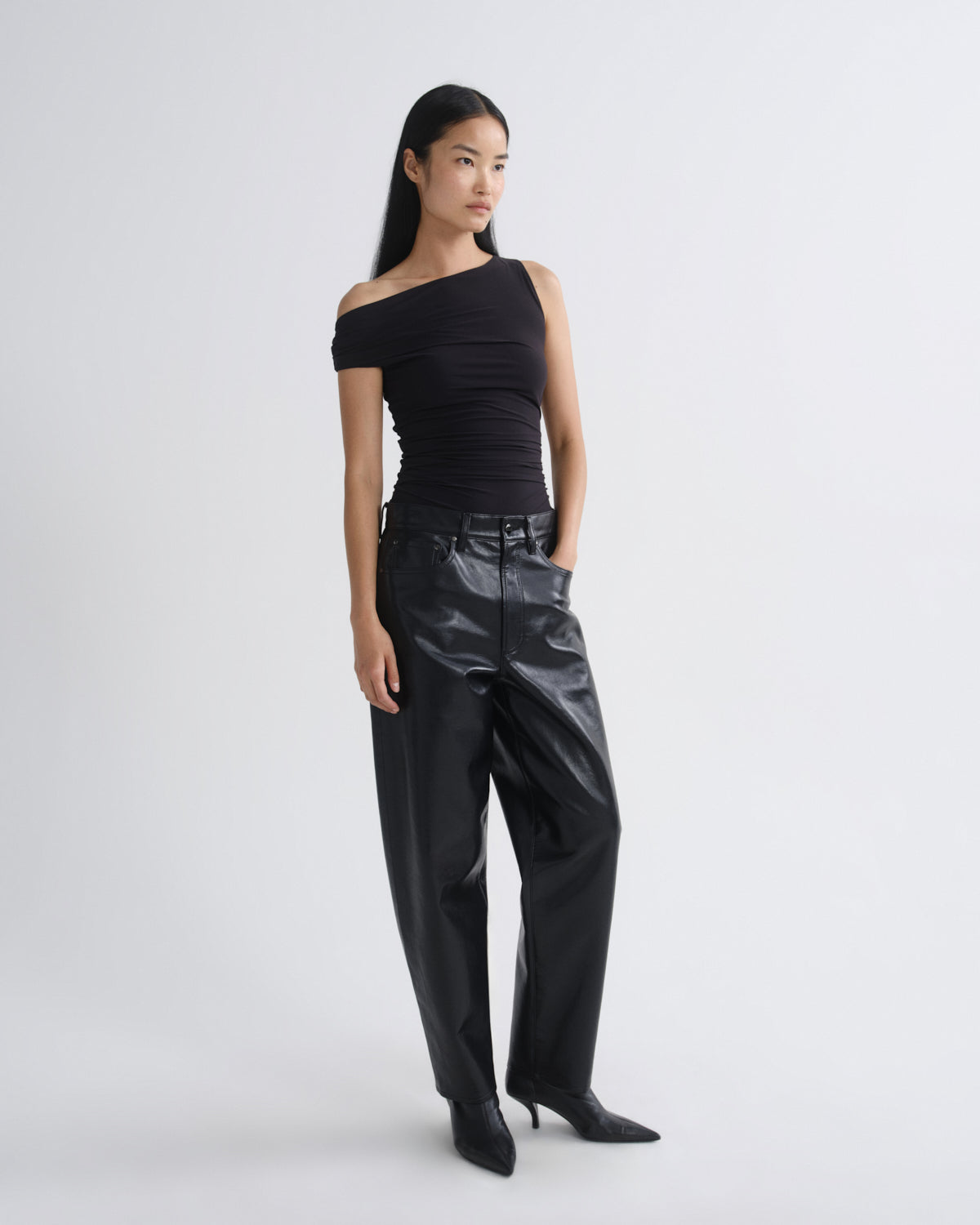 Woman wearing a black off-shoulder top and black leather pants on a white background