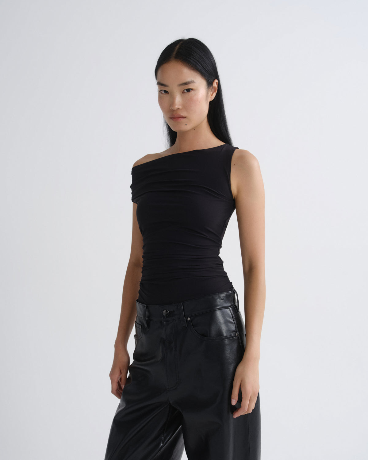 Woman wearing a black one-shoulder top and black pants on a white background