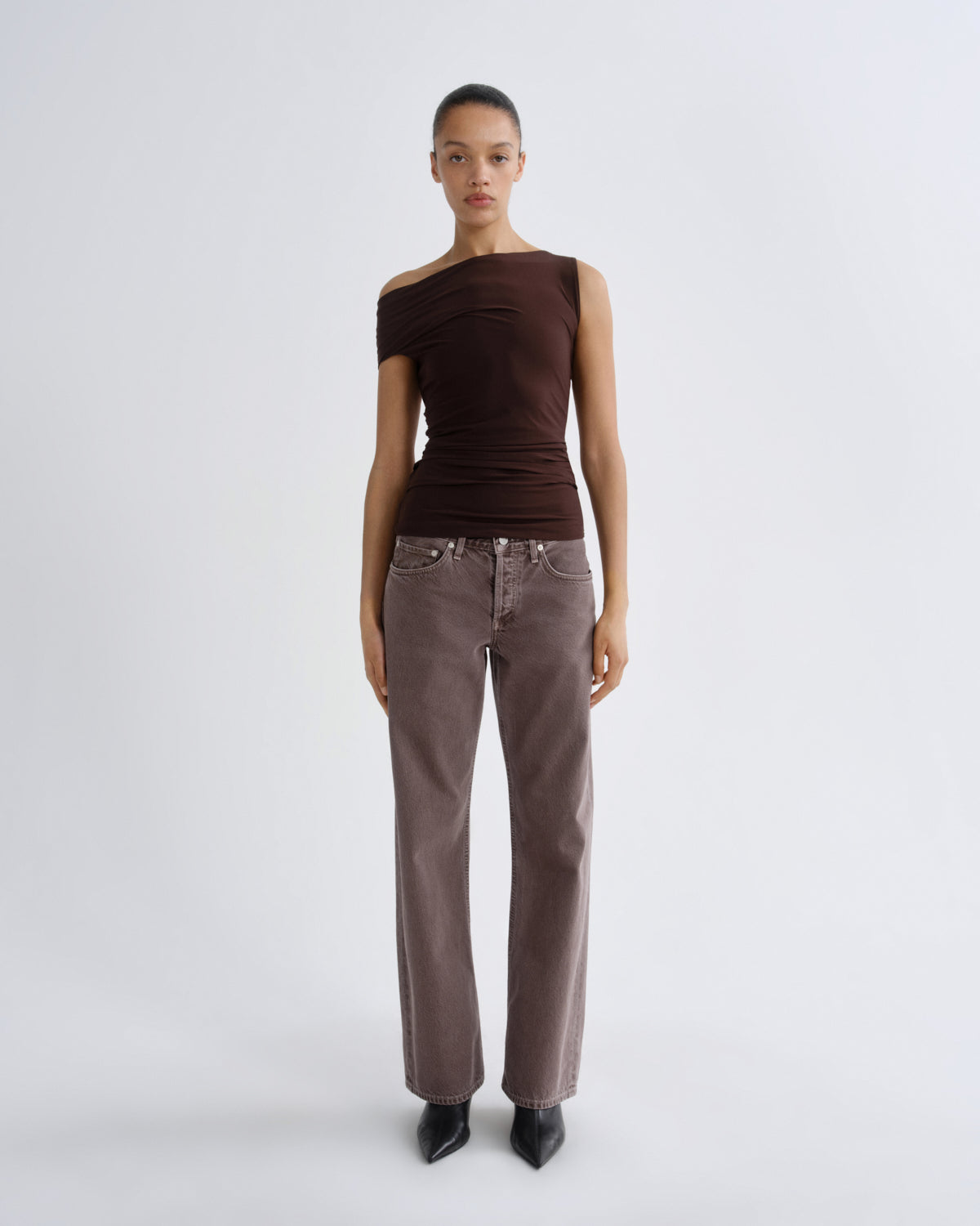 Woman wearing a brown top and jeans on a white background