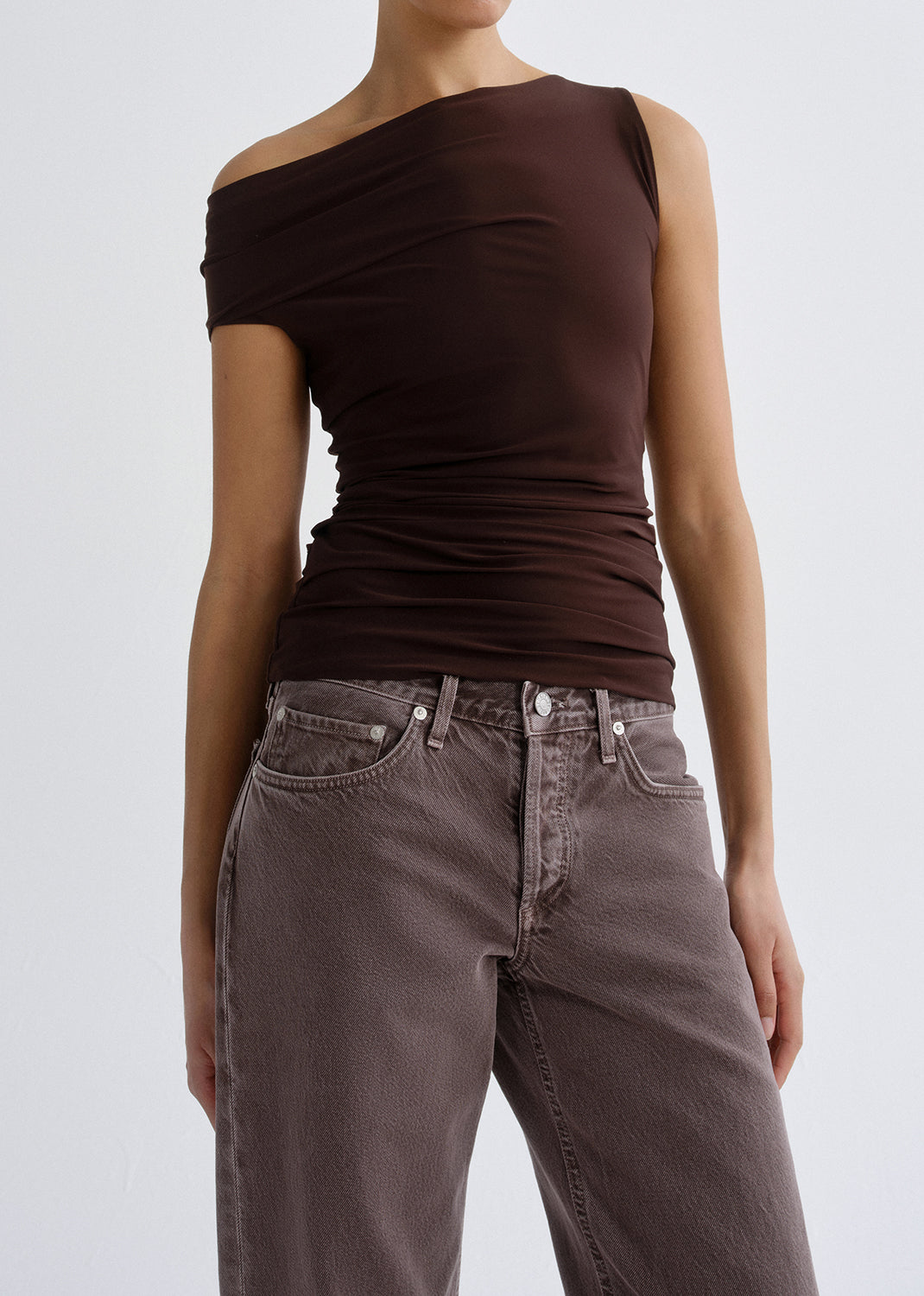 Person wearing a dark brown one shoulder top on a grey background.