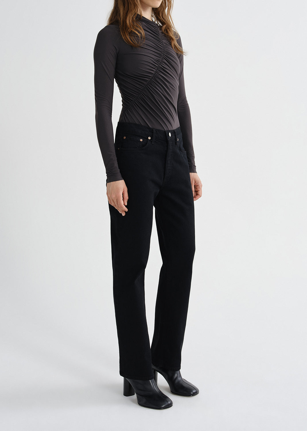 Person wearing a charcoal long sleeve ruched mock neck top with black skinny jeans on a grey background.
