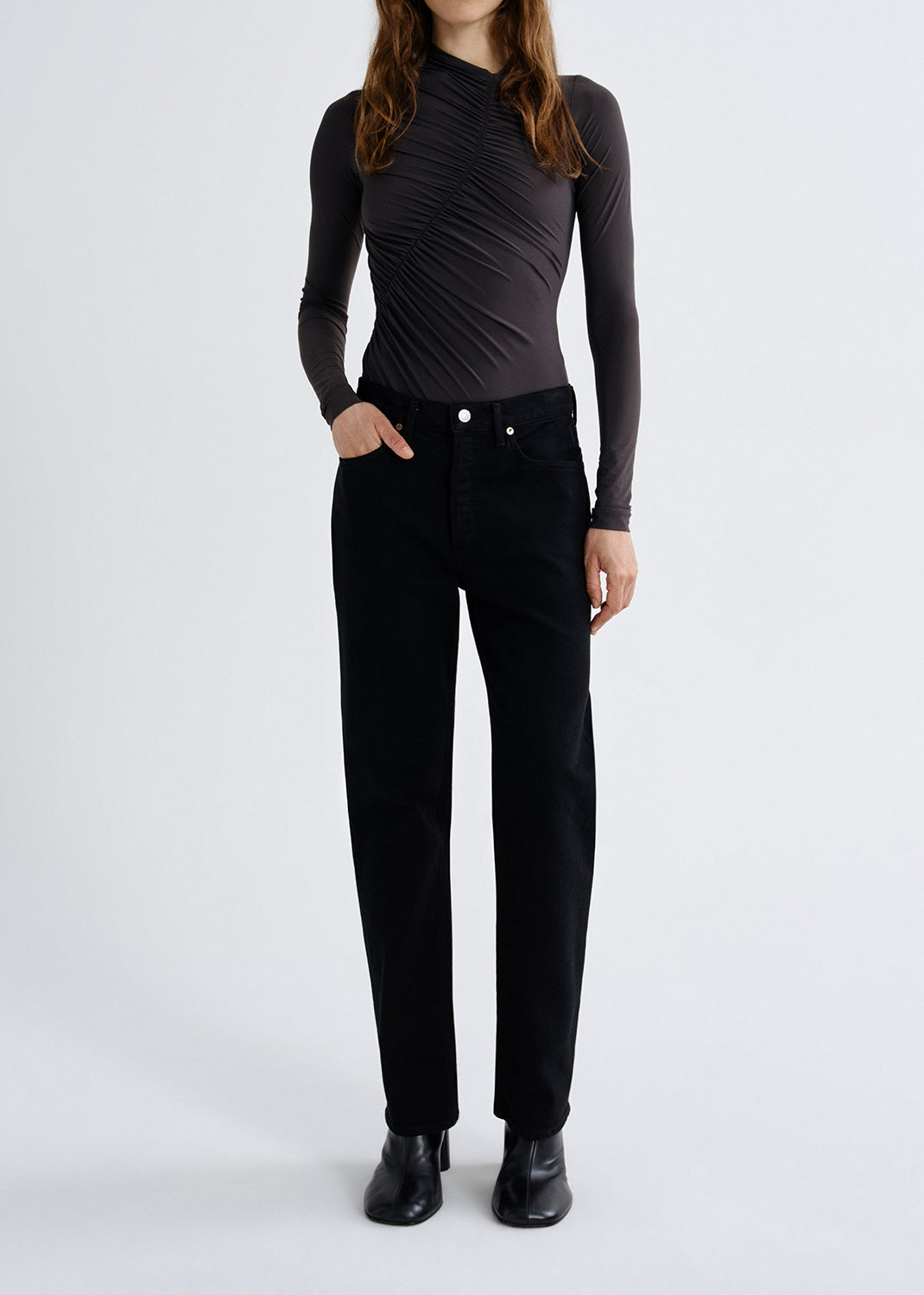Person wearing a charcoal long sleeve ruched mock neck top with black skinny jeans on a grey background.