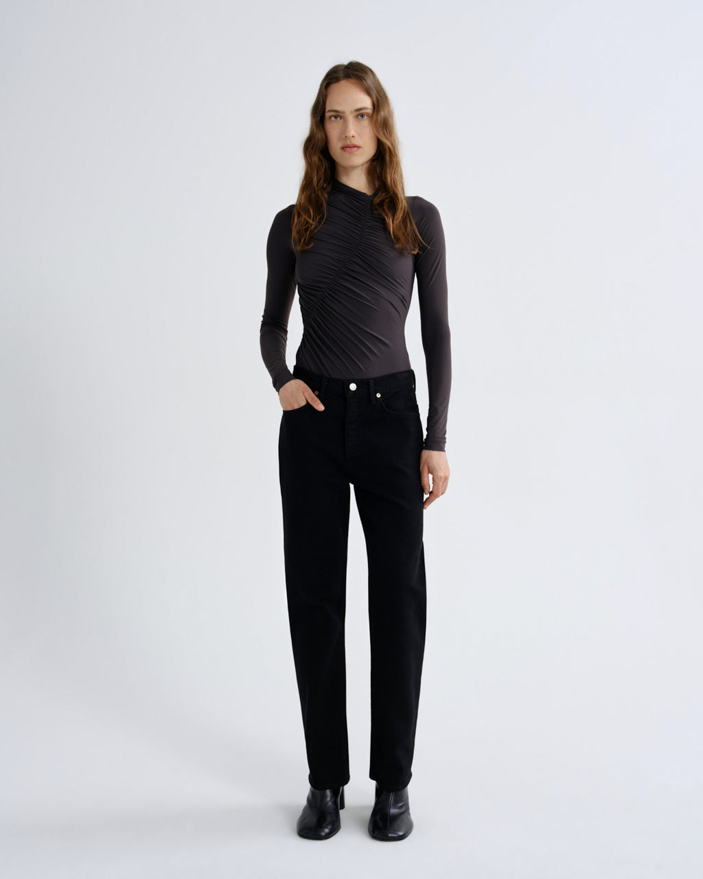Person wearing black pants and a brown top on a white background