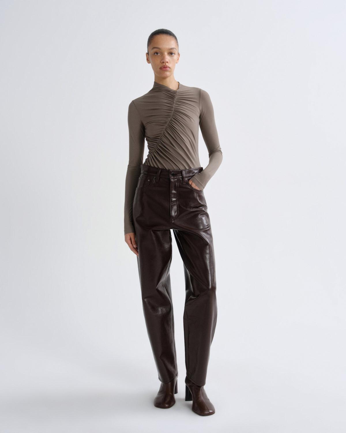 Person wearing a brown ruched top and leather pants on a white background