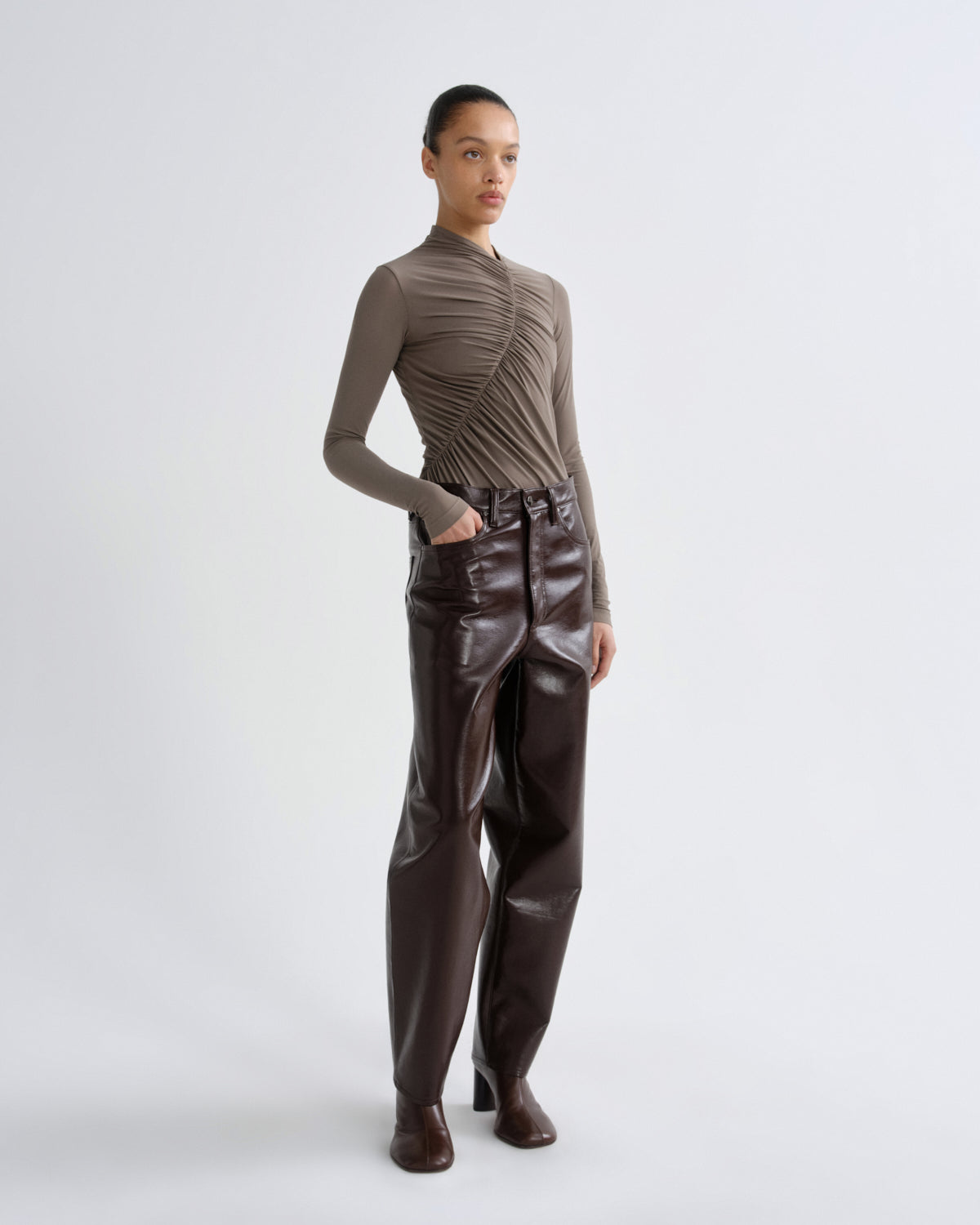 Person wearing a brown ribbed sweater and leather pants on a white background