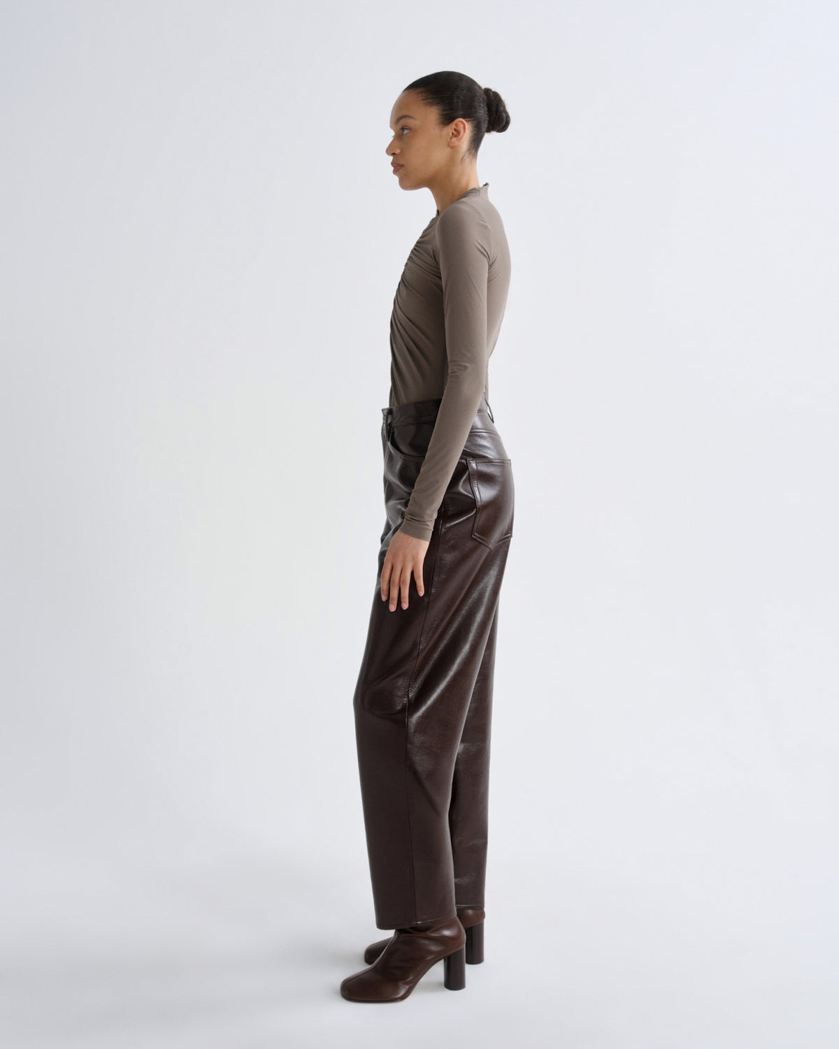 Woman wearing a brown long-sleeve top and dark brown pants on a white background