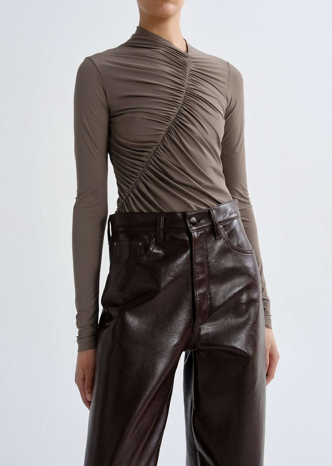 Person wearing a taupe long sleeve ruched mock neck top on a grey background.