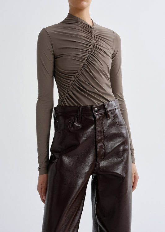 Person wearing a taupe long sleeve ruched mock neck top on a grey background.