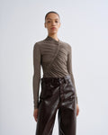 Person wearing a brown ruched top and dark brown leather pants on a white background