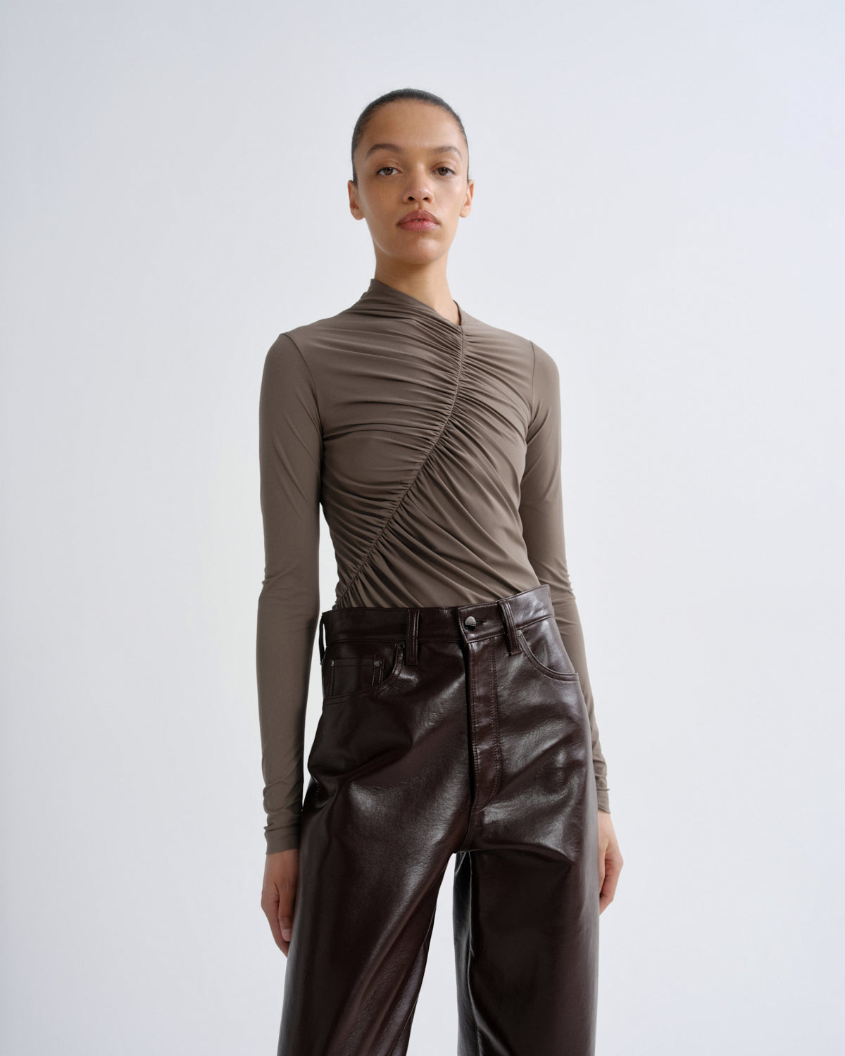 Person wearing a brown ruched top and dark brown leather pants on a white background