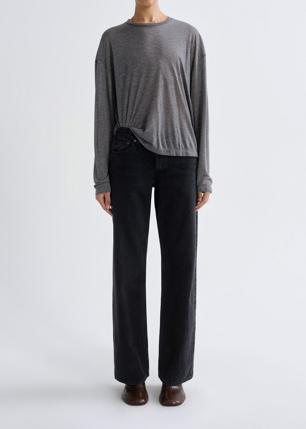 Person wearing a grey long-sleeve top and black pants on a grey background